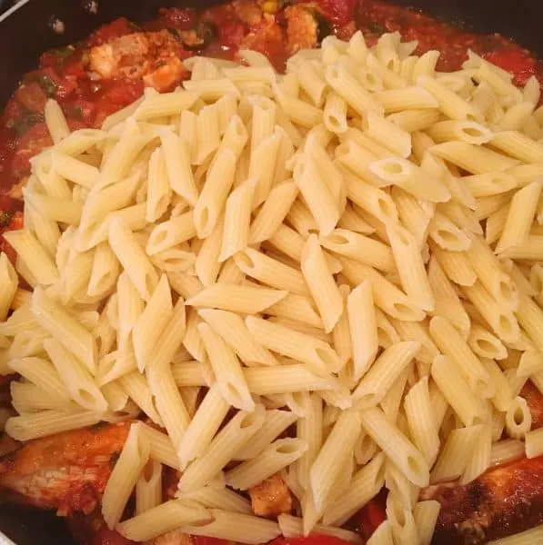 addition of penne pasta to sauce with chicken