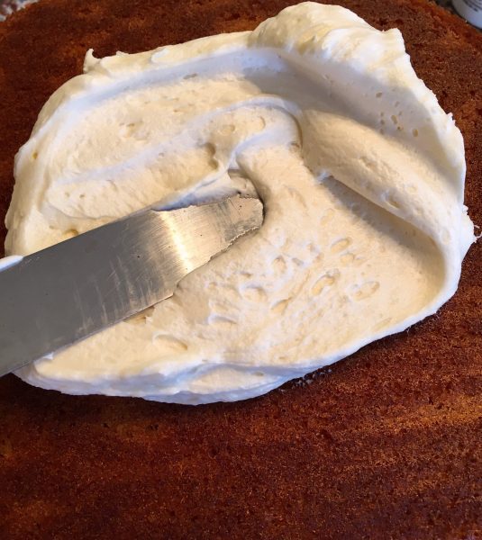 spreading cream cheese frosting on pumpkin cake