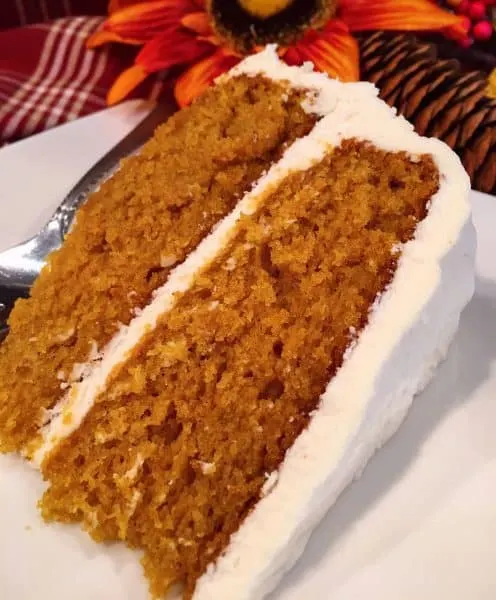 slice of pumpkin cake with cream cheese frosting on white plate