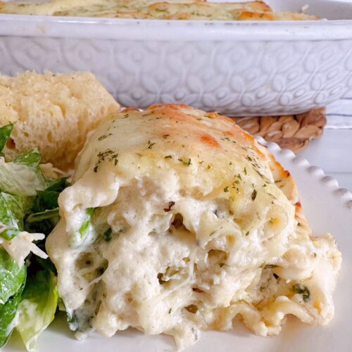 Spinach Alfredo Chicken Lasagna Roll up on a dinner plate with salad and garlic bread.