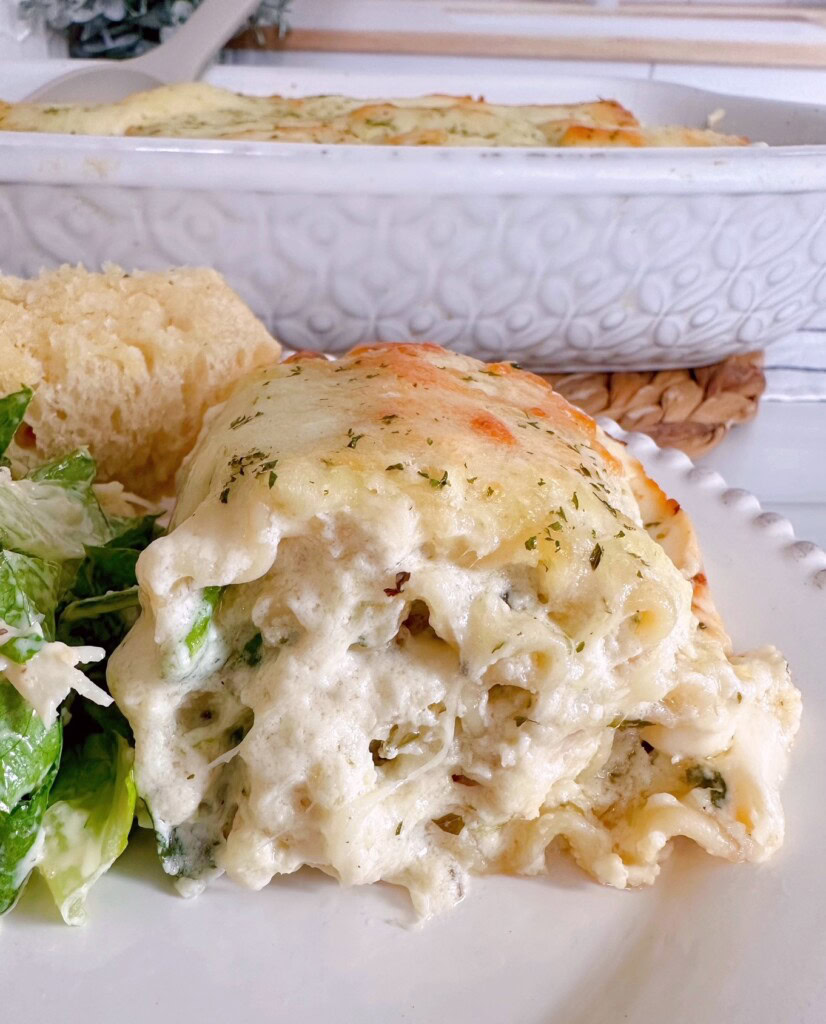 Spinach Alfredo Chicken Lasagna Roll up on a dinner plate with salad and garlic bread.
