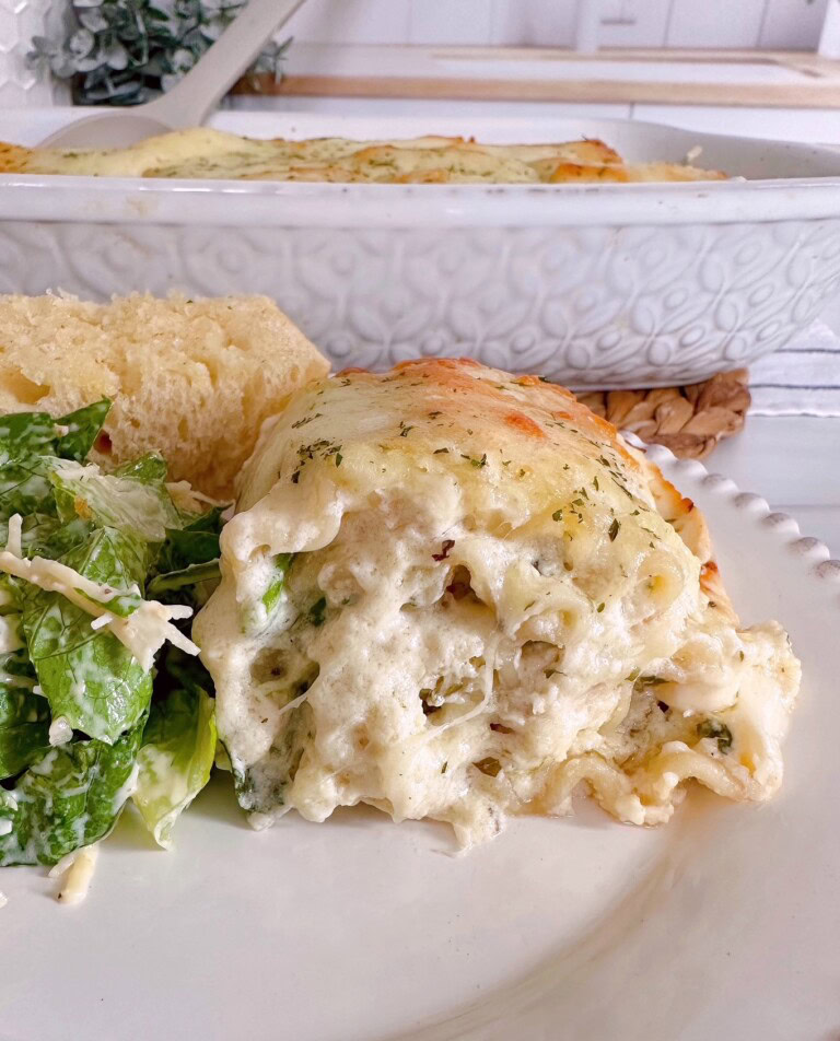 Serving of Chicken Alfredo Lasagna Roll Up on a dinner plate with salad and bread.