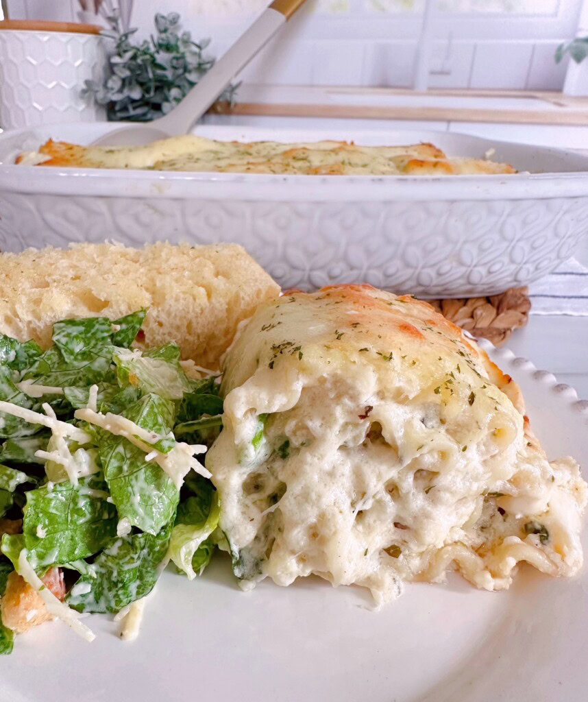 Chicken spinach alfredo roll-up on a plate with salad and garlic bread.