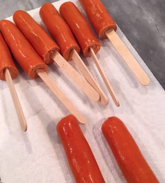 hot dogs are cut in half with sticks in them ready to dunk in corn meal