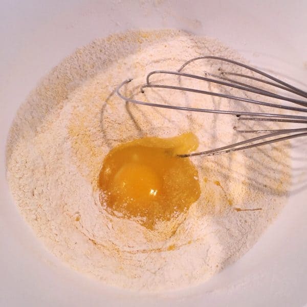 Corn meal, flour, egg, and bowl with a whisk