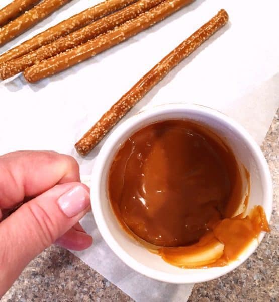 Cup of melted caramel and pretzel sticks for dipping