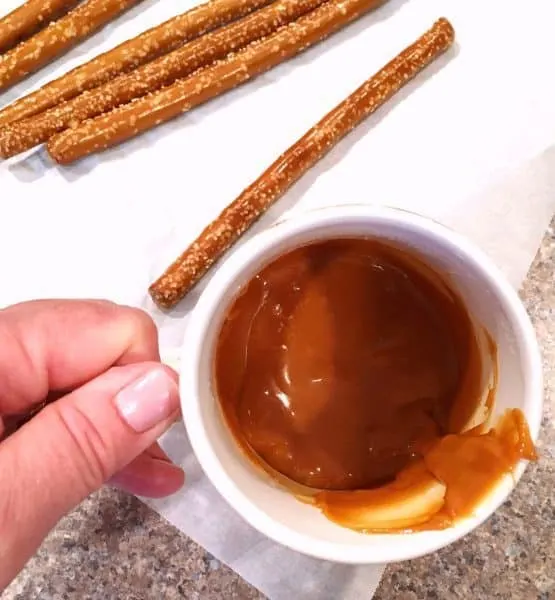 Cup of melted caramel and pretzel sticks for dipping