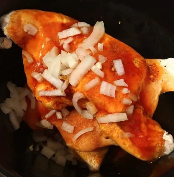 chicken breast, onion, and enchilada sauce in the slow cooker