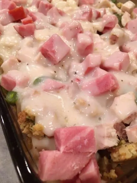 pouring cream gravy sauce over meat and stuffing in casserole dish