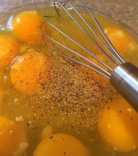 Eggs, salt and pepper in a bowl being whisked.
