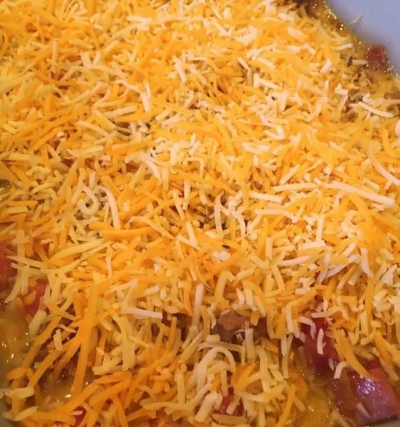 grated cheese on top of egg mixture in casserole dish for breakfast casserole