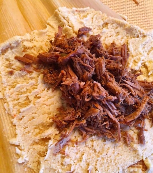 Meat filling on top of masa in corn husks