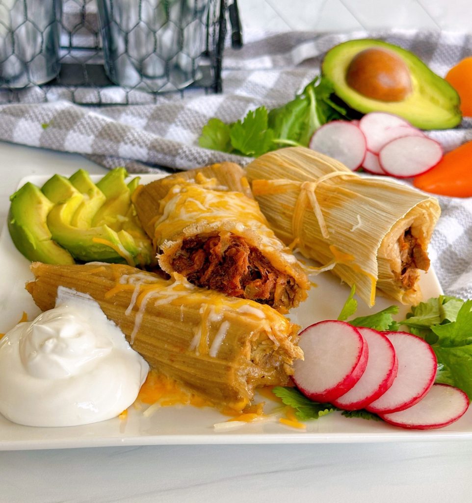 Photo of Tamales on a plate with toppings and fixings.