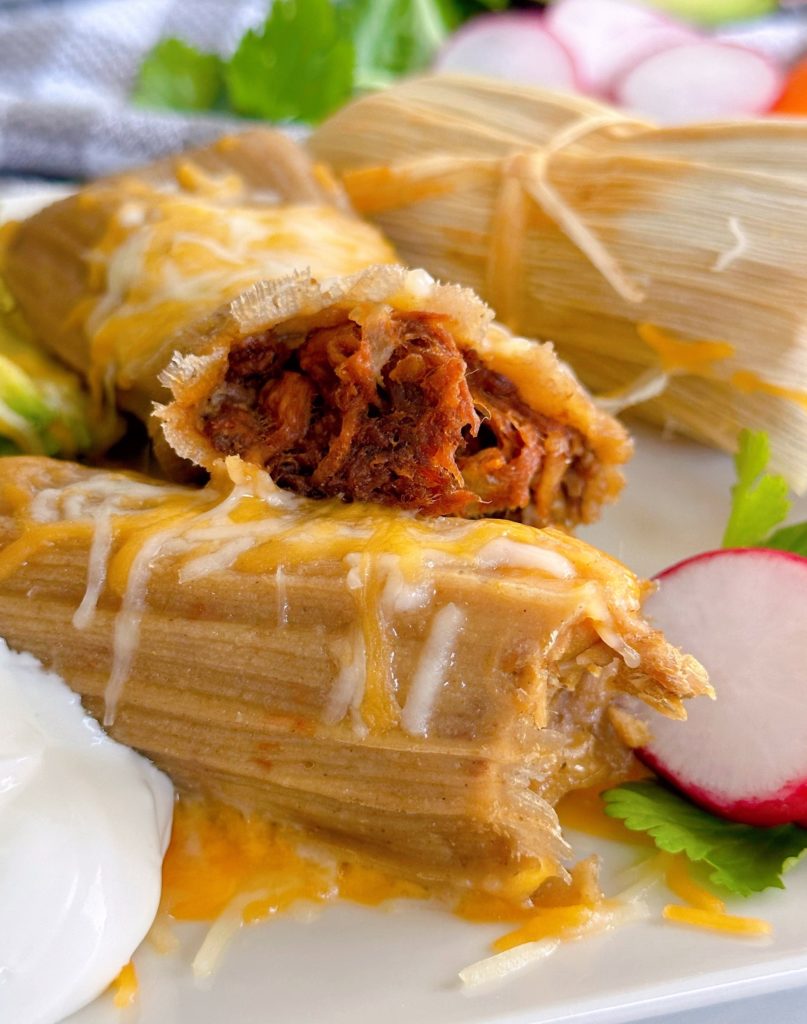 Close-up photo of a beef tamale on a plate with a pork tamale.