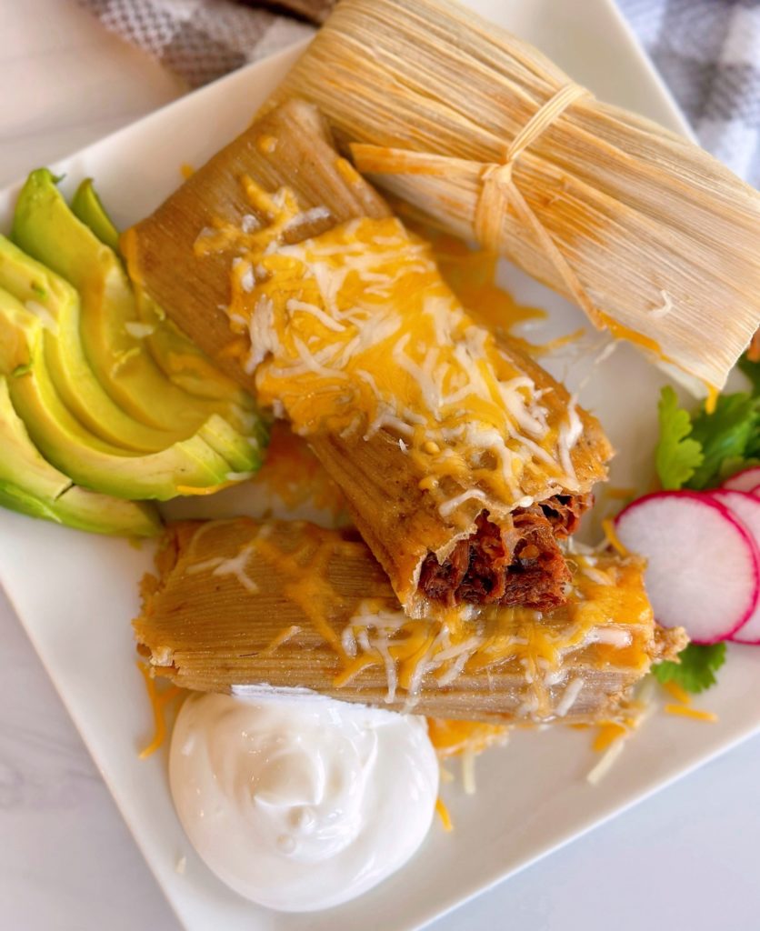 Homemade Christmas Tamales on a plate with avocado and radishes, sour cream.