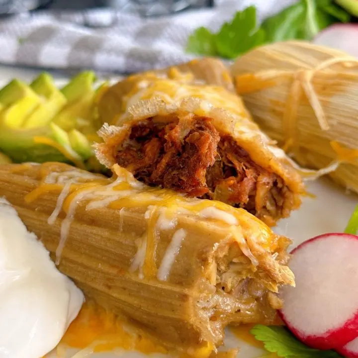 Pork and Beef tamales on a plate with cheese and sour cream.
