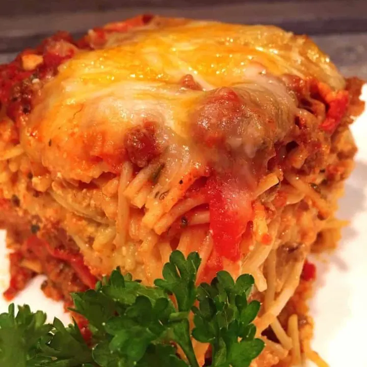 Meat lovers baked spaghetti serving with fresh parsley on a white serving dish.