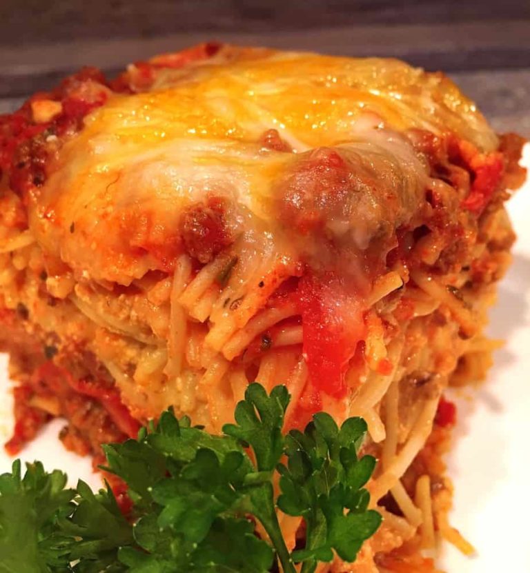 Meat lovers baked spaghetti serving with fresh parsley on a white serving dish.