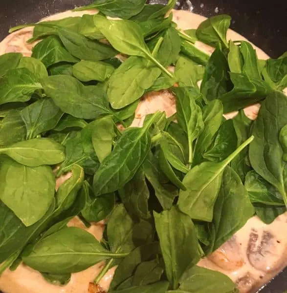 Fresh spinach leaves added to creamy garlic sauce