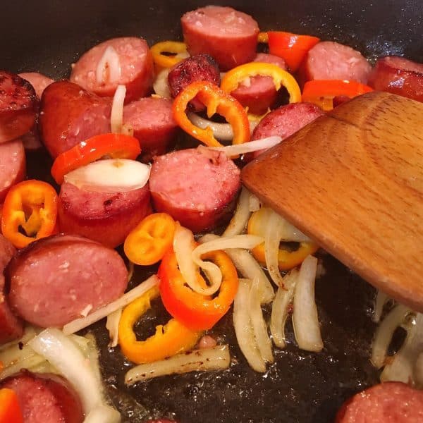 Adding onions and peppers with sausage in the skillet