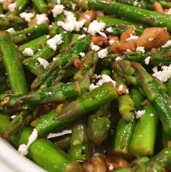 Sauteed Asparagus in white serving bowl with toasted walnuts and sprinkled with Feta Cheese