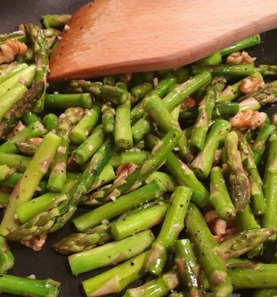 Cut up Asparagus spears sauteed in a skillet with chopped walnuts and seasonsings