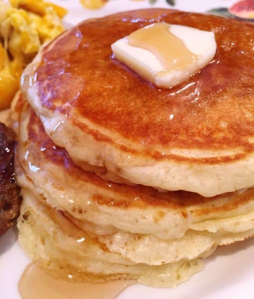 Plate piled high with light fluffy buttermilk pancakes topped with rich maple syrup