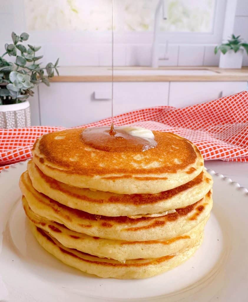 Stack of pancakes with syrup pouring over the top of them.