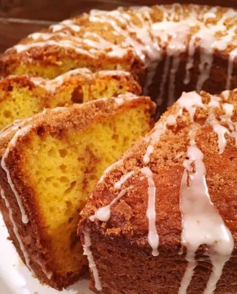 Round Bundt Cake with slices leaning on cinnamon coffee cake drizzled with vanilla icing.