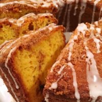 Large bundt yellow cake with swirls of cinnamon filling and a light streusel crumb topping and drizzles of vanilla glaze.