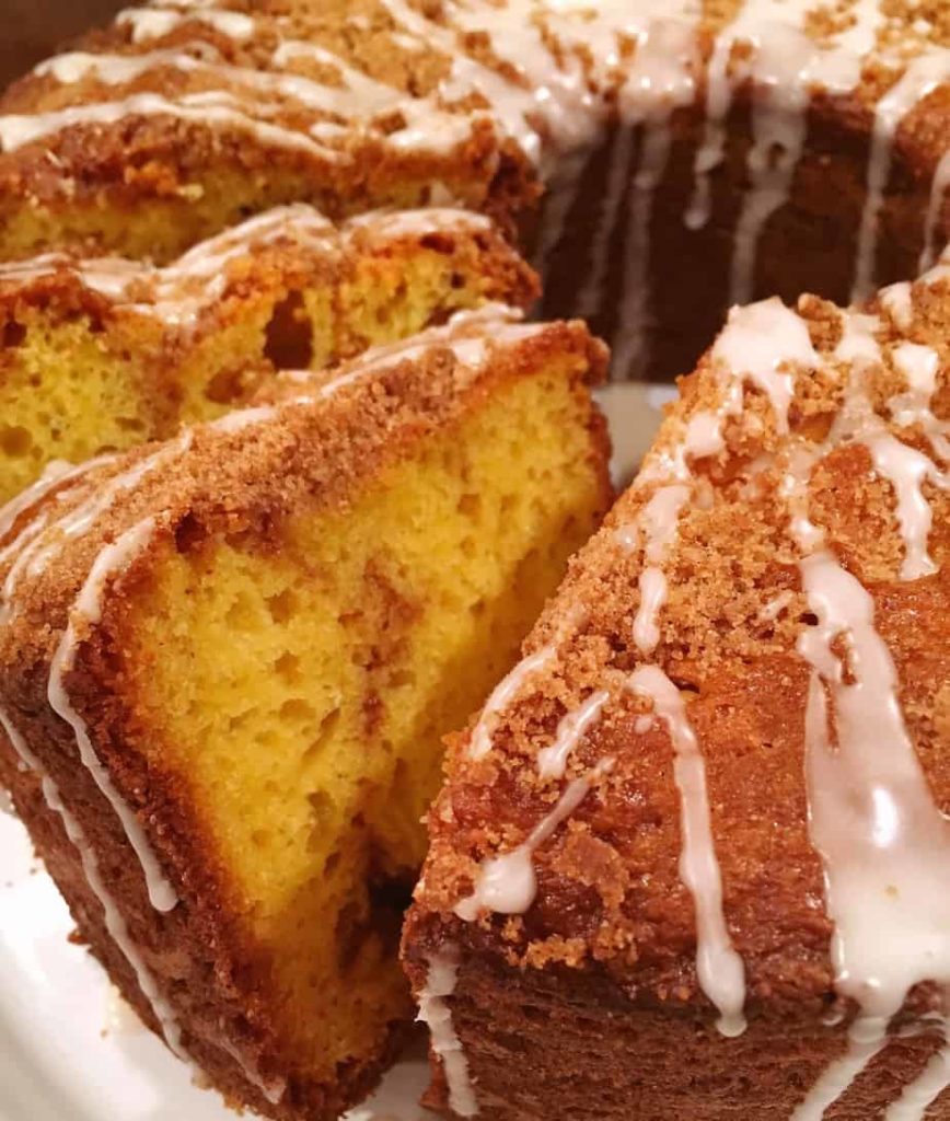 Large bundt yellow cake with swirls of cinnamon filling and a light streusel crumb topping and drizzles of vanilla glaze.
