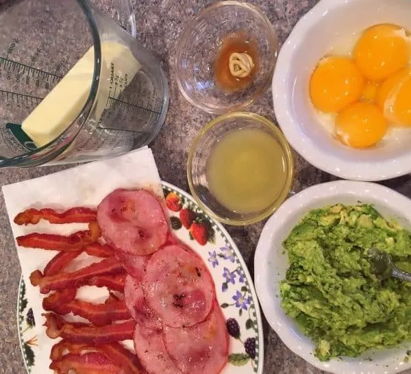 Bowls and plates with Egg Benedict Ingredients, egg yolks, lemon juice, bacon, smashed avocado, butter