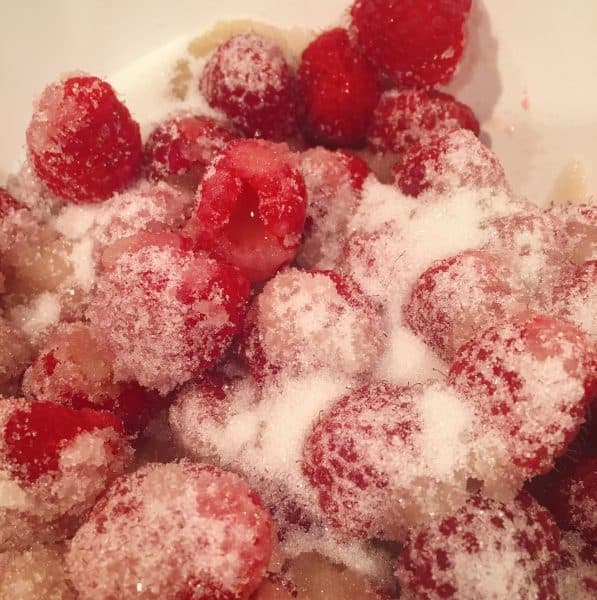 Bowl filled with fresh raspberries, apple juice, and sugar