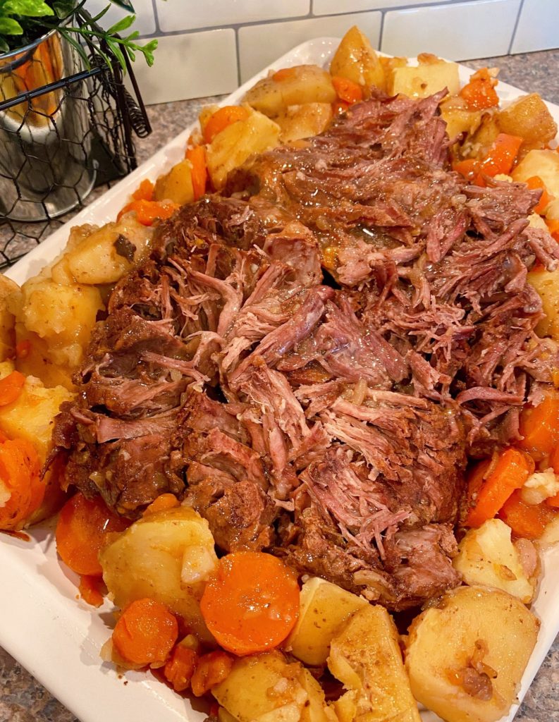 Best Pot Roast on a platter shredded with potatoes and carrots surrounding it.