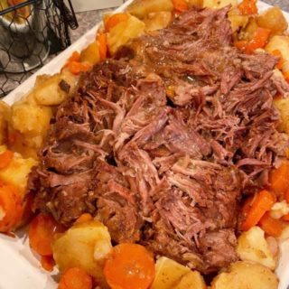 Best Pot Roast on a platter shredded with potatoes and carrots surrounding it.