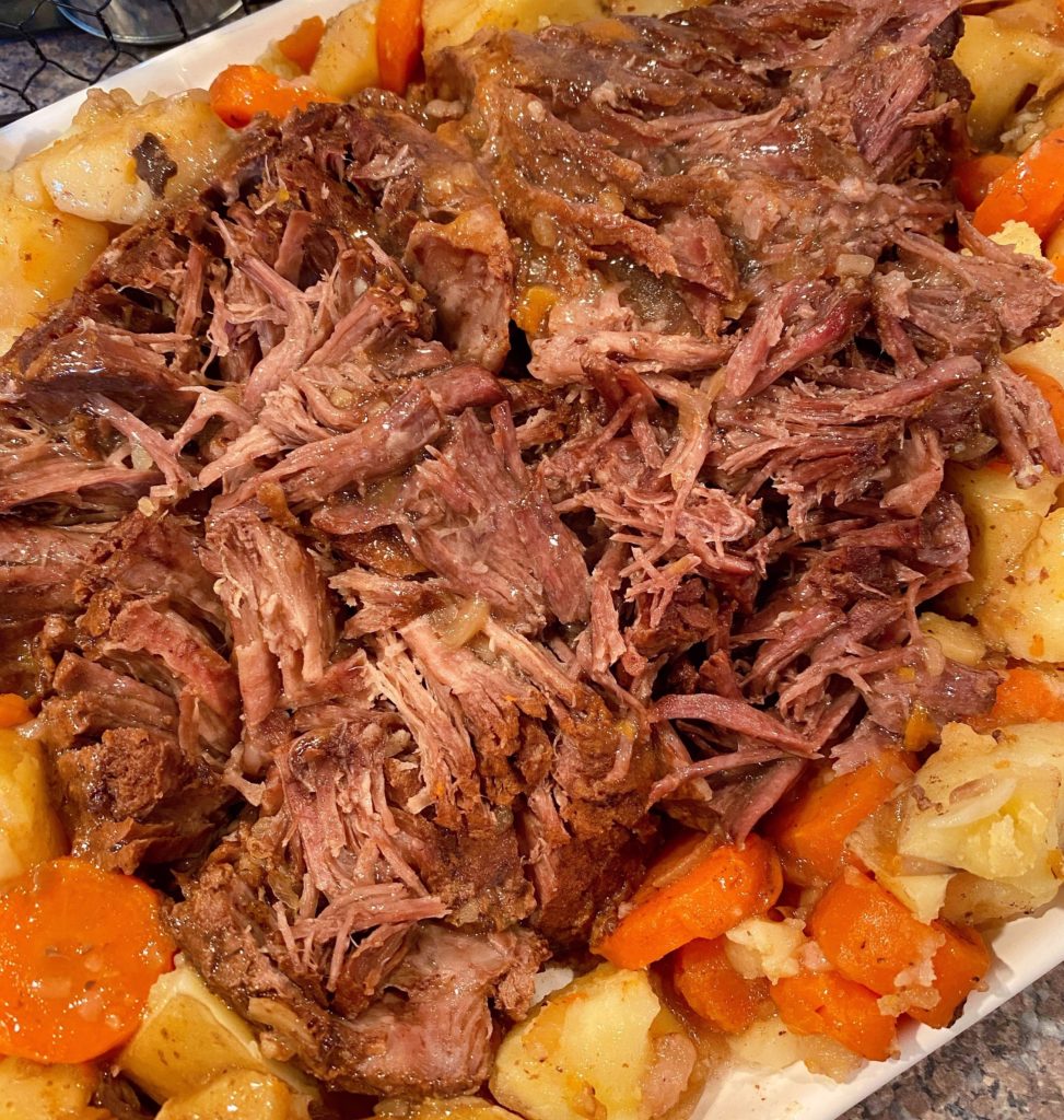 Best Pot Roast shredded on a serving platter with potatoes and carrots surrounding it.