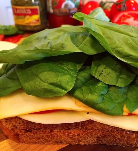 Building of Italian Grilled Cheese adding Munster Cheese, Spinach, and Fresh Basil