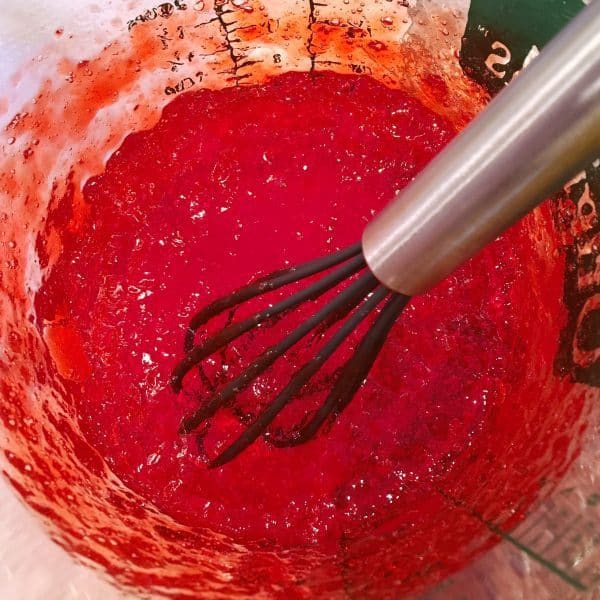 Glass Measuring cup with dissolved thickened jello and small whisk.