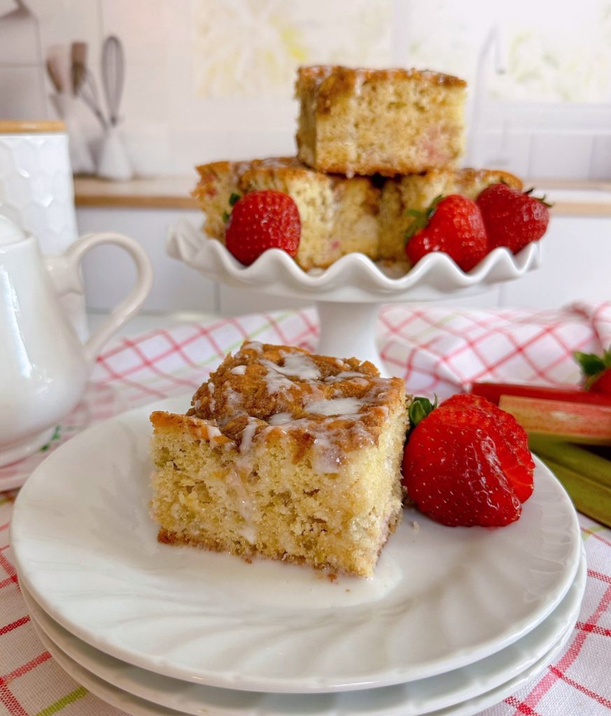 Rhubarb Coffee Cake serving on a plage with a stack of cake slices on a cake stand.