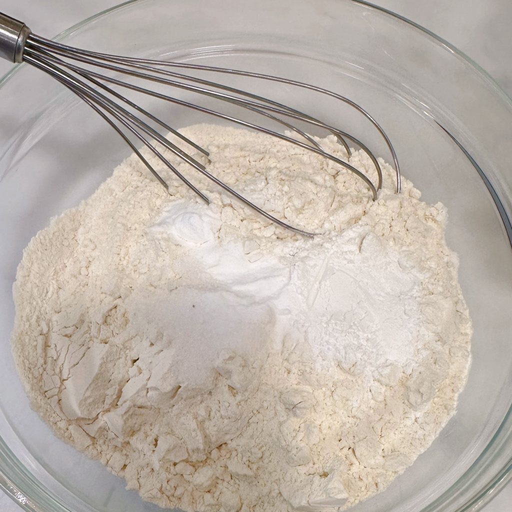 Dry ingredients in a glass bowl being whisked together.