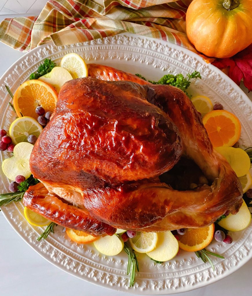 Roasted Turkey on a white platter with fruit slices surrounding it.