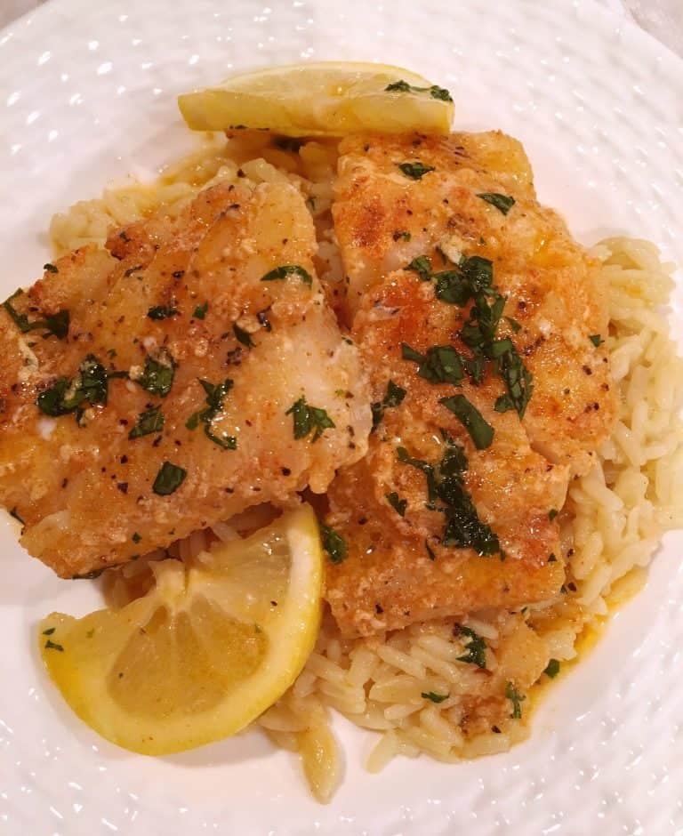 Buttered Cod over Rice on a white plate with lemon wedges.
