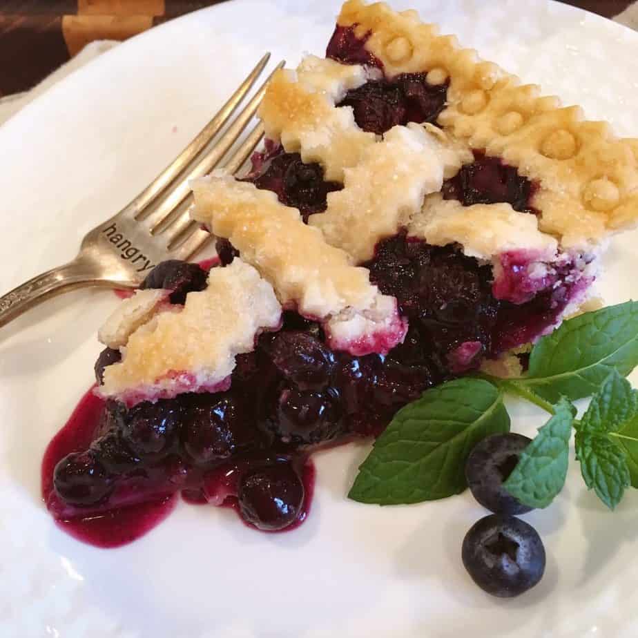 Slice of classic blueberry pie on a white plate.