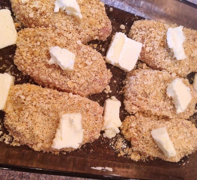 Breaded pork chops with dabs of butter on top and around them in a 9 x 13 baking pan.
