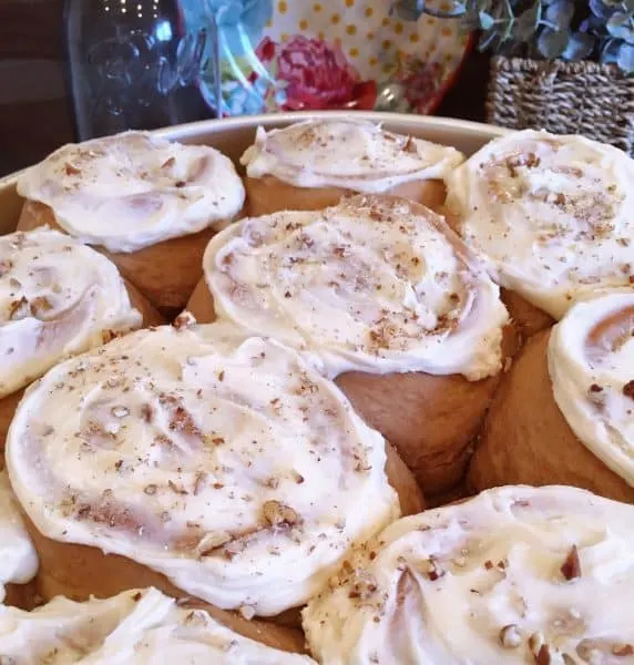 Carrot Cake Mix Cinnamon Rolls with cream cheese frosting and toasted pecans sprinkled on top.