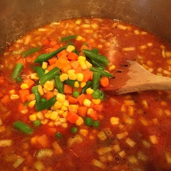 Adding a bag of vegetables to soup mix in pot