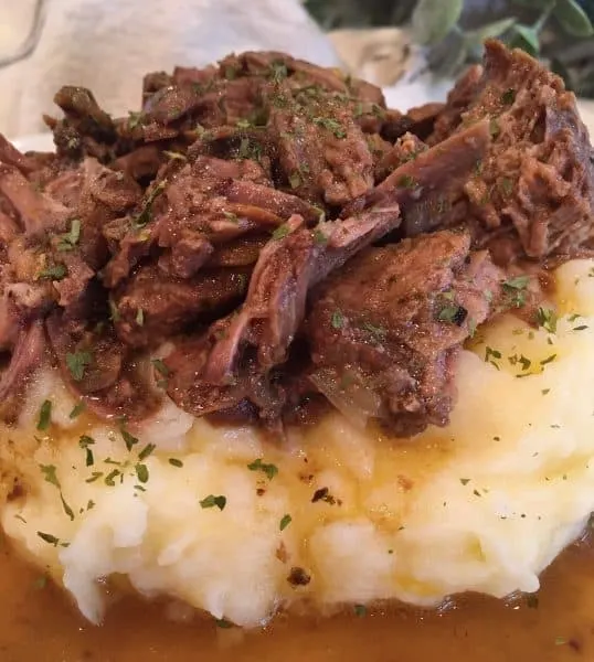 Mississippi Pot Roast and Gravy on a bed of Garlic Cheddar Mashed Potatoes with fresh chopped parsley.