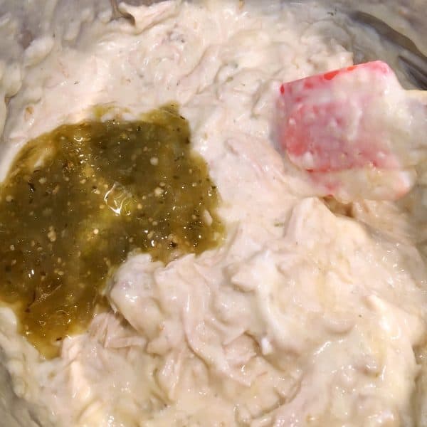 Half cup of Salsa Verde being added to slow cooker enchilada chicken mixture.