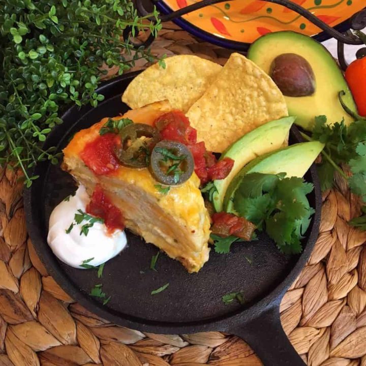 Over head shot of slice of chicken layered enchilada casserole. Topped with a drizzle of salsa, jalapeno slices, and a scoop of sour cream.