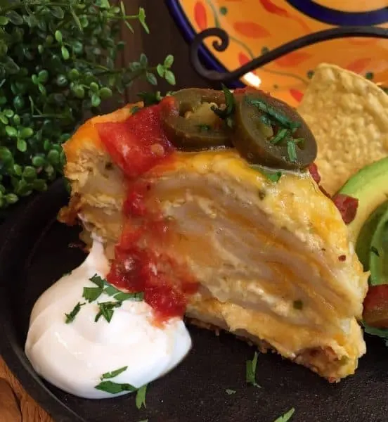 Close-up of slow cooker layered chicken enchilada casserole topped with salsa. It's warm and delicious, served with avocado slices and sour cream.
